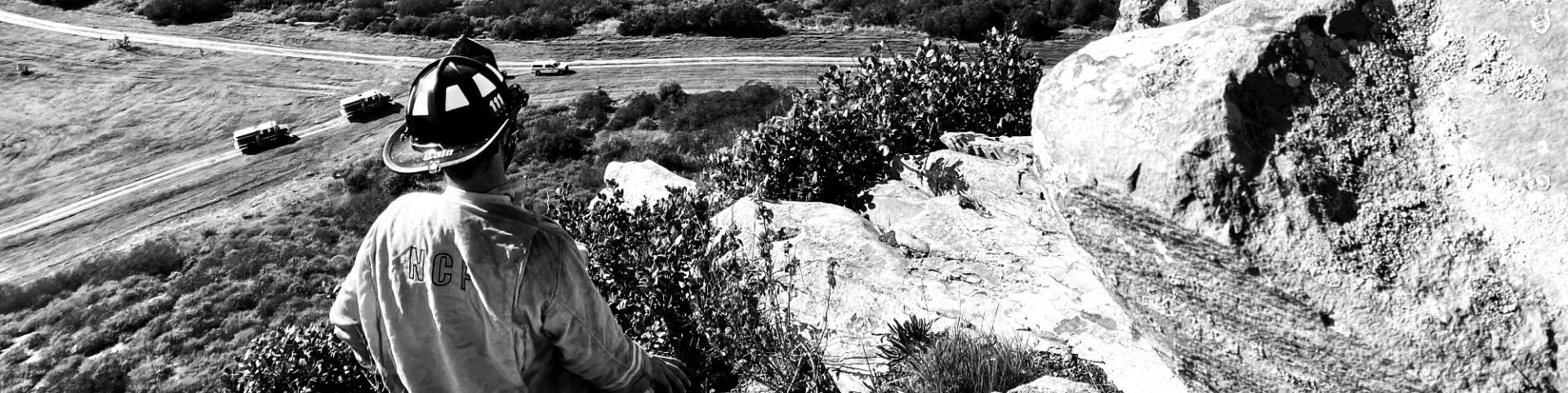 Firefighter looking over cliff at road below with trucks