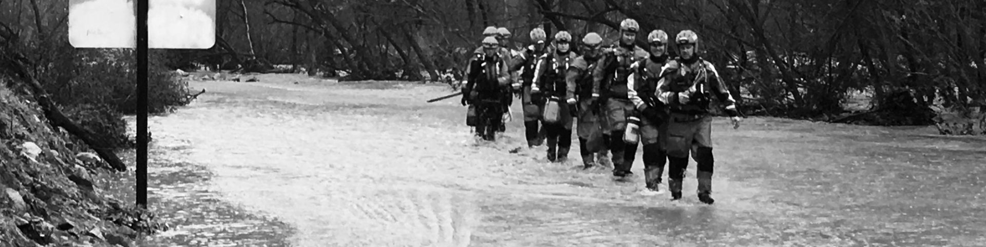 Row of firefighters walking through flooded street