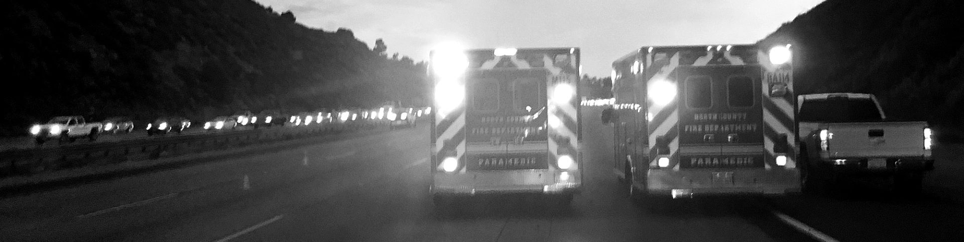Two ambulances drive down highway with emergency lights on